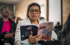 Durante un evento, una mujer lee un ejemplar del libro Las voces del Crea