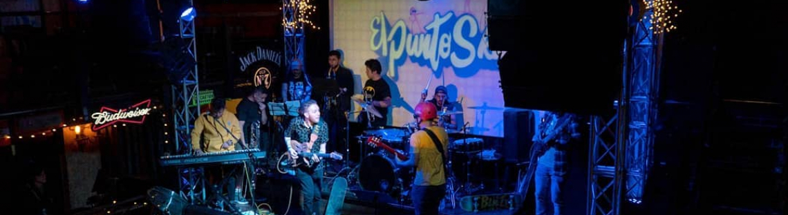 Agrupación musical conformada por nueve hombres realizando un concierto en un espacio cerrado