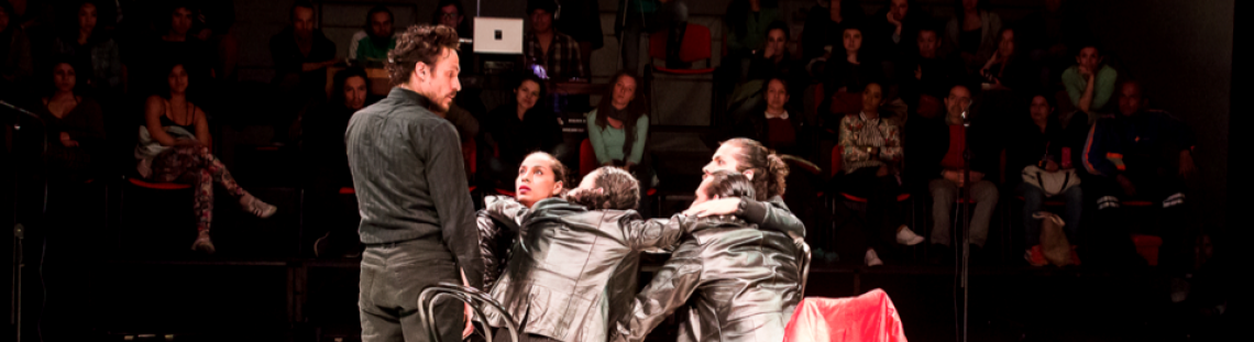 Cuatro actores que hacen parte de una escena de teatro con público al fondo