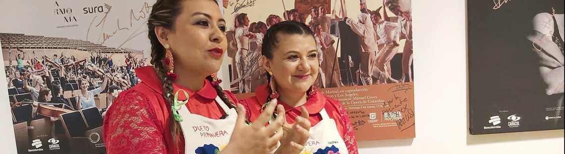 Dos mujeres peinadas con trenzas, vestidas con blusa roja y un delantal