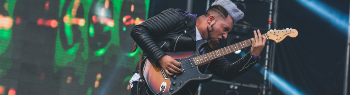 Hombre joven saltando mientras toca una guitarra eléctrica en una presentación musical