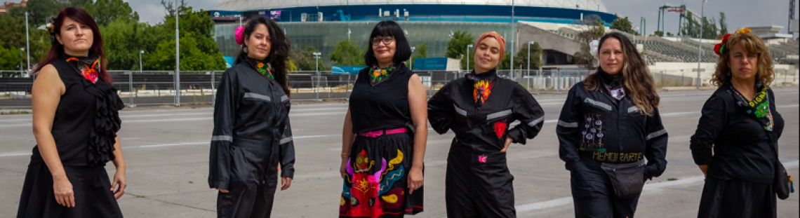 Seis mujeres vestidas con prendas negras y bordadas posando de pie de día.