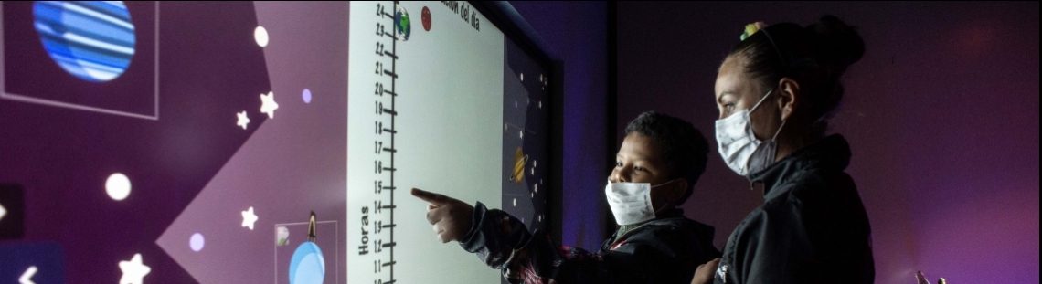 Dos personas con una pantalla táctil en el Planetario. 