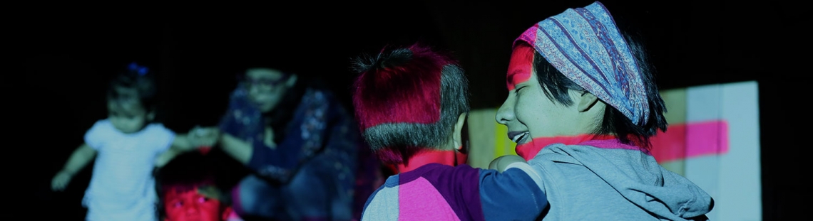 Niños en un cuarto oscuro alumbrados por luces de colores. 