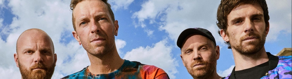 Integrantes de Coldplay con cielo azul y nubes de fondo. 