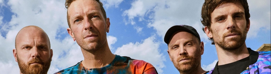 Integrantes de Coldplay con cielo azul y nubes de fondo. 