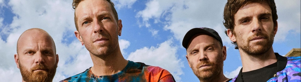 Integrantes de Coldplay con cielo azul y nubes de fondo. 