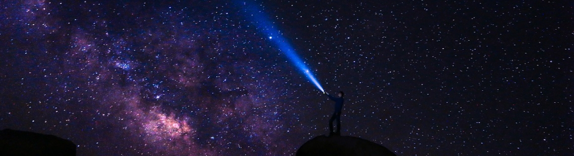 Cielo estrellado con señor apuntando al cielo con linterna. 