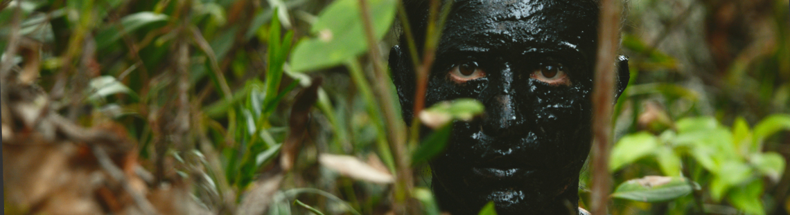 Rostro pintado totalmente de negro en medio de la vegetación