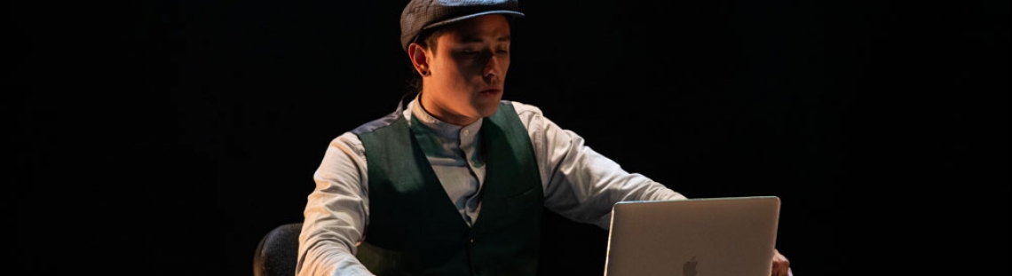 obra de teatro con joven sentado en escritorio viendo computador