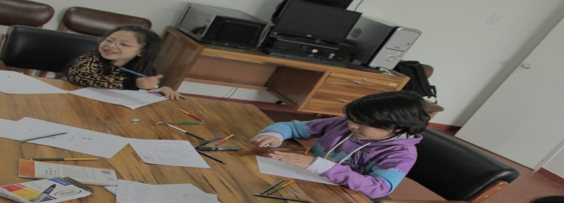 dos niños en una mesa usan colores para plasmar sus ideas en un papel