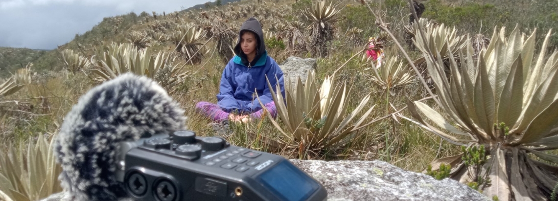 Imagen de mujer escuchando la naturaleza en montaña de Bogotá con un micrófono en frente.