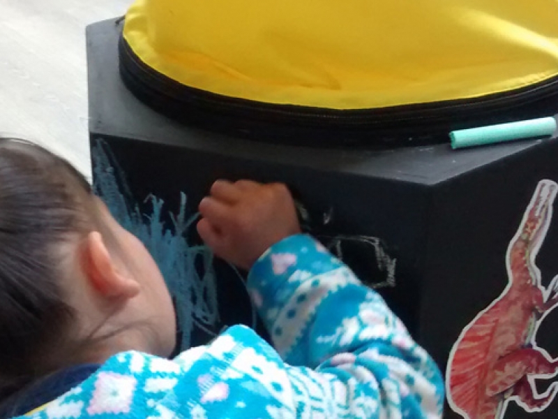 Niña dibujando con tiza de colores un cubo negro de madera.