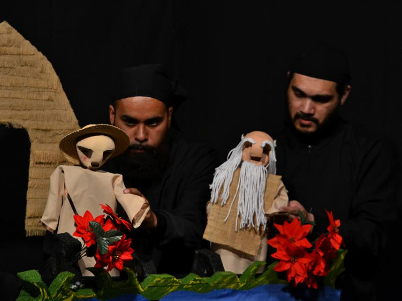 Hombres manejando los títeres en el escenario con flores