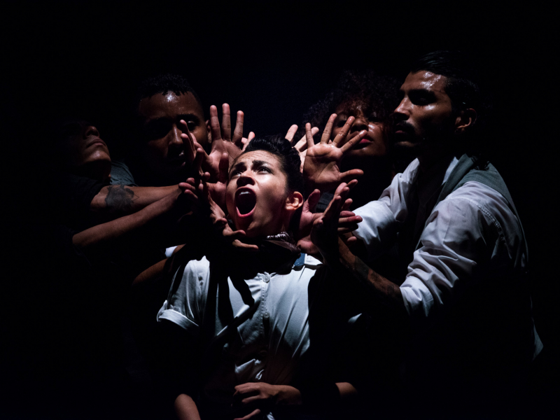 Varios hombres en el escenario, uno de ellos en actitud de grito rodeado por las manos de los otros.