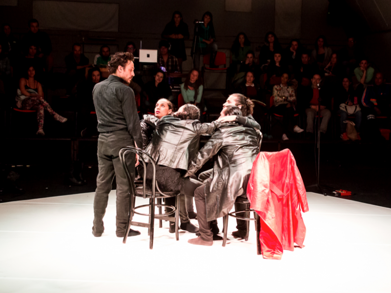 Cuatro actores que hacen parte de una escena de teatro con público al fondo