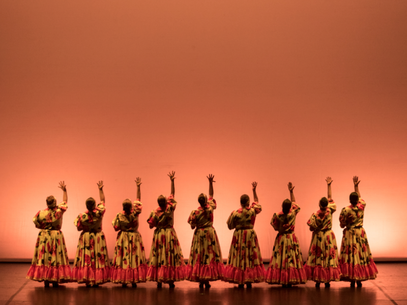 Mujeres  danzando en el escenario con trajes coloridos.