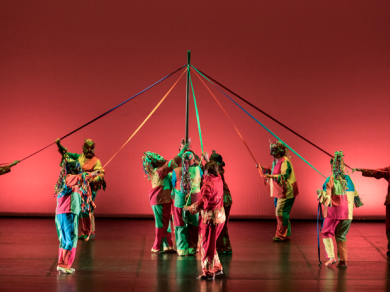 Grupo de bailarines con  lazos de colores entrelazados en el escenario