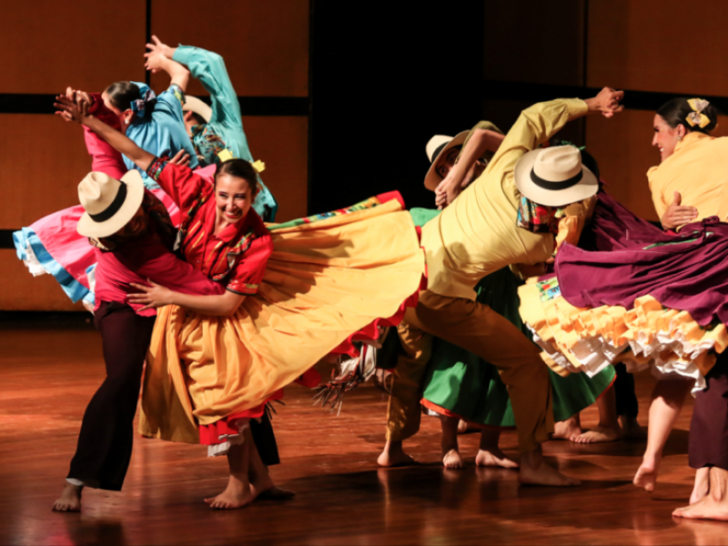 Personas de trajes coloridos y alegres bailando en un escenario