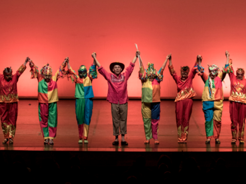 Personas en el escenario con trajes coloridos y brazos en alto