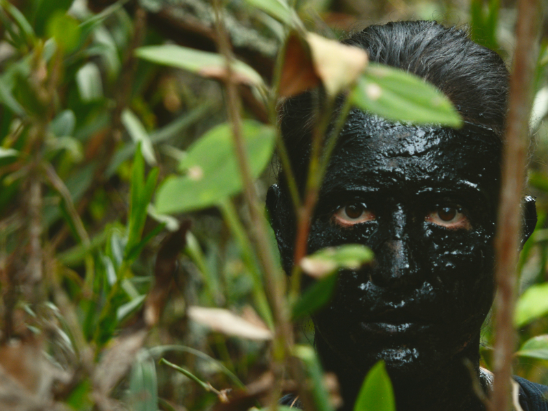 Rostro pintado totalmente de negro en medio de la vegetación