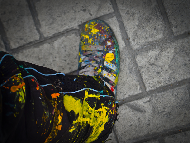 Zapato y pantalón de grafitero sobre baldosa pintados de muchos colores por pintura caída