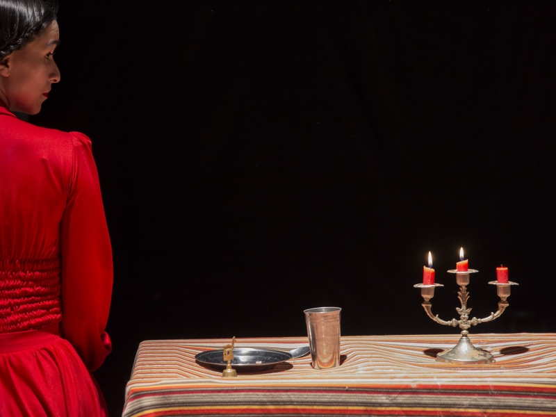 Mujer vestida de rojo al lado de una mesa con plato, vaso y velas.