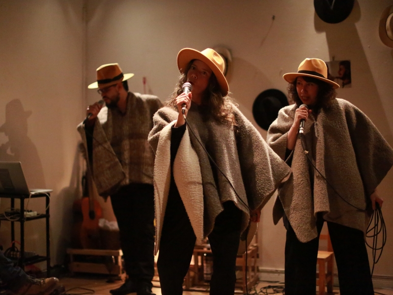 Dos mujeres y un hombre con sombreros y microfonos en escena