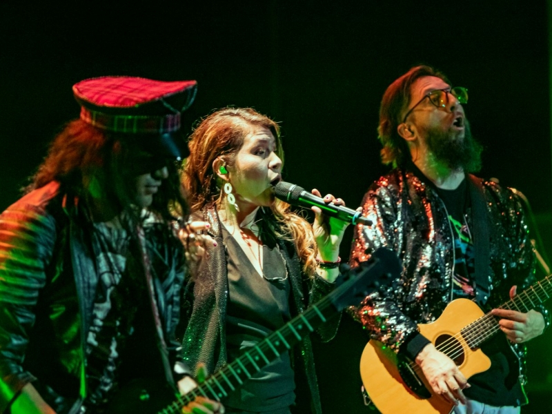 Una mujer cantando y dos hombres a su lado tocando guitarra