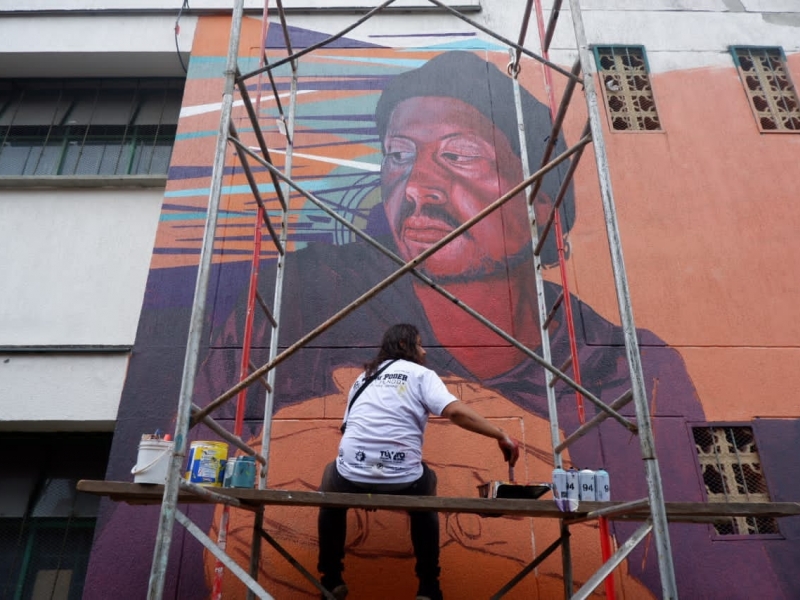 Persona pinta un gran mural de día.