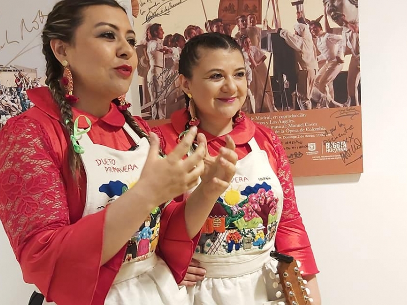 Dos mujeres peinadas con trenzas, vestidas con blusa roja y un delantal