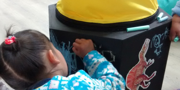 Niña dibujando con tiza de colores un cubo negro de madera.