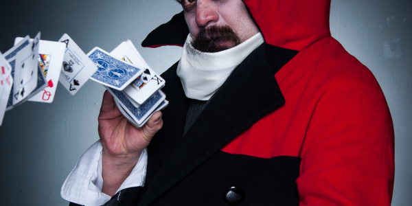 Hombre con capa roja y sombrero jugando con las cartas de un naipe.