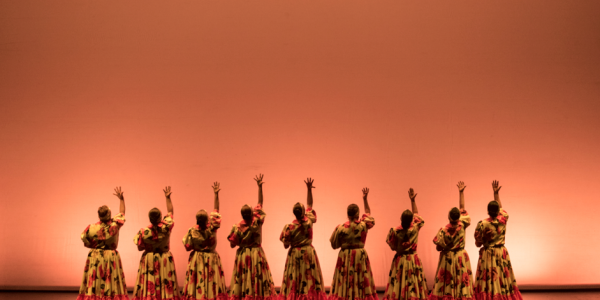 Mujeres  danzando en el escenario con trajes coloridos.