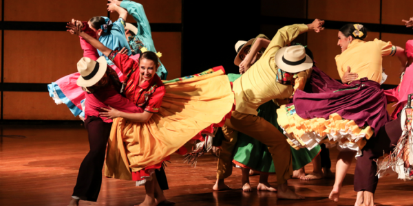 Personas de trajes coloridos y alegres bailando en un escenario