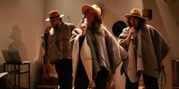 Dos mujeres y un hombre con sombreros y microfonos en escena