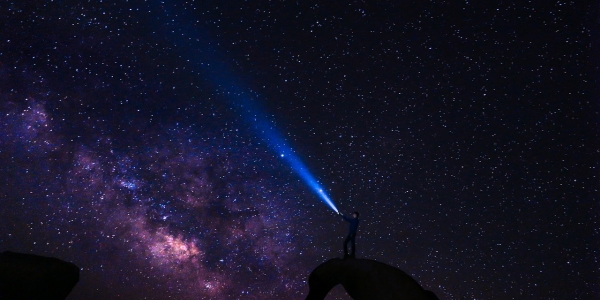 Cielo estrellado con señor apuntando al cielo con linterna. 