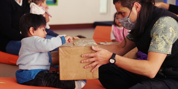 Niño jugando con una caja y un artista del Programa Nidos