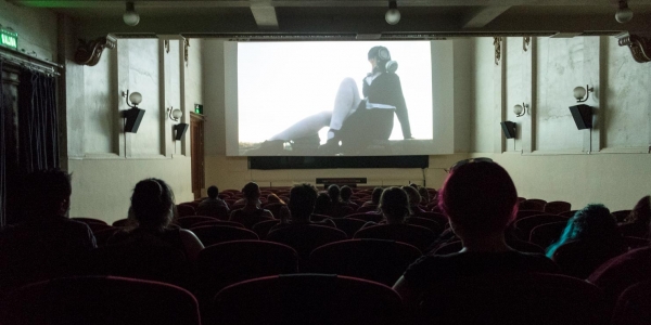 Personas en una sala de cine con una proyección de una mujer en blanco y negro. 