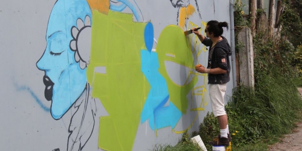 Hombre pinta con brocha un mural en el exterior de día