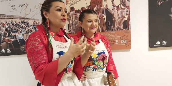 Dos mujeres peinadas con trenzas, vestidas con blusa roja y un delantal