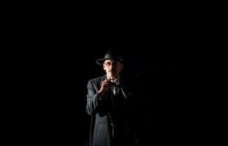 Hombre de negro fumando en escenario oscuro