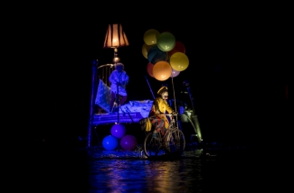 Mujer en cama flotante con globos y hombre con bicicleta sobre el lago.