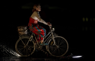 Actriz con traje de colores en bicicleta sobre el lago.
