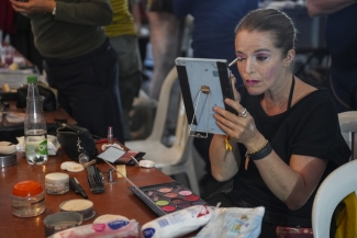 Actriz maquillandose frente a un espejo de mano y maquillaje sobre una mesa.