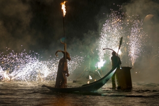 Actir con máscara en góndola sobre lago y muchas luces.