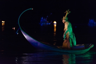 Actor con reflejos de luz verde en góndola azul sobre lago.