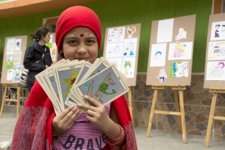 Niña disfrazada de lectora del tarot, vestida de rojo con cartas grandes.